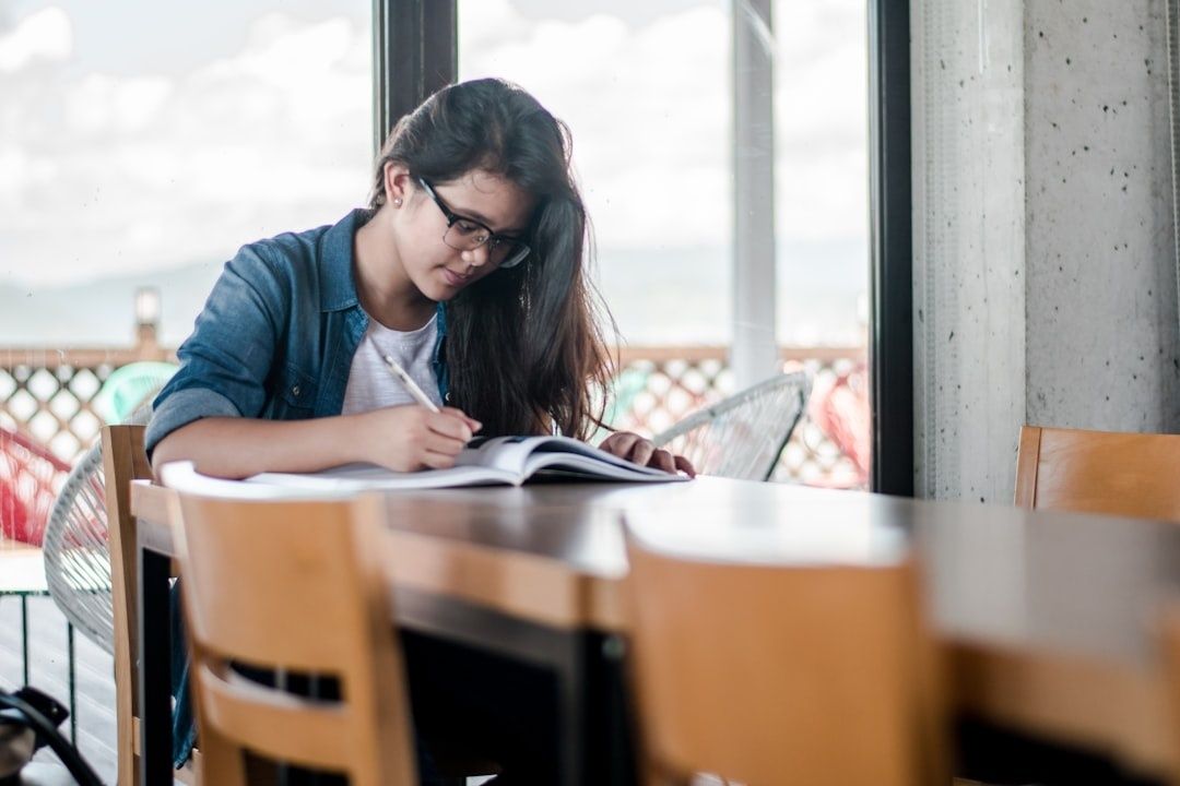 Student sitter vid ett bord och skriver i en kursbok nära ett fönster